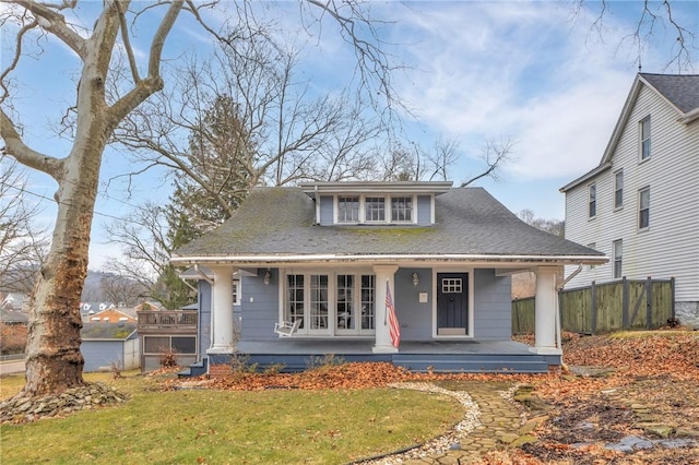 bungalow-style house with covered porch, roof with shingles, fence, and a front yard