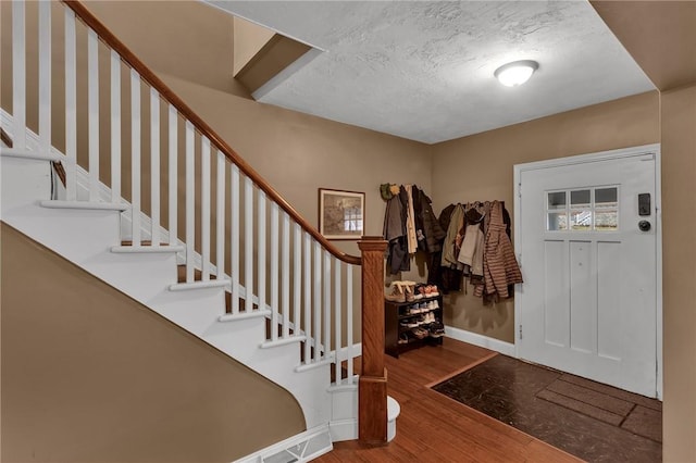 entrance foyer featuring a textured ceiling, wood finished floors, stairs, and baseboards