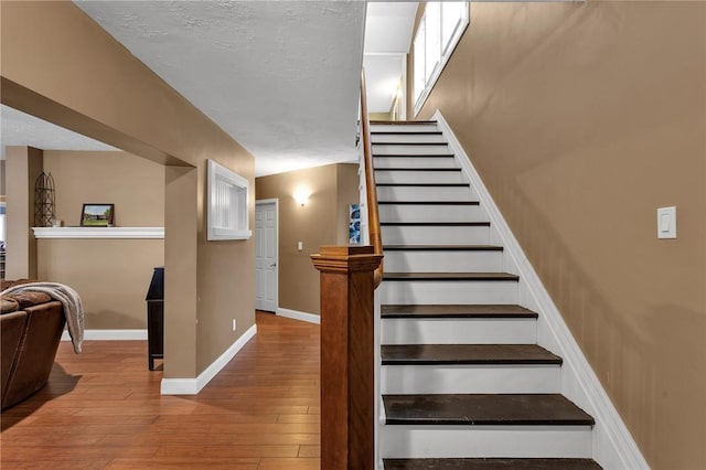 stairway with a textured ceiling, baseboards, and hardwood / wood-style flooring