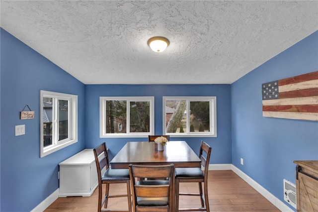 dining space featuring a textured ceiling, baseboards, and wood finished floors