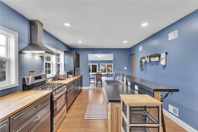 kitchen with butcher block countertops, a sink, visible vents, wall chimney range hood, and stainless steel gas stove