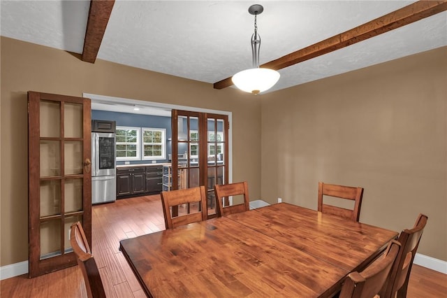 dining area featuring beamed ceiling, a textured ceiling, baseboards, and wood finished floors