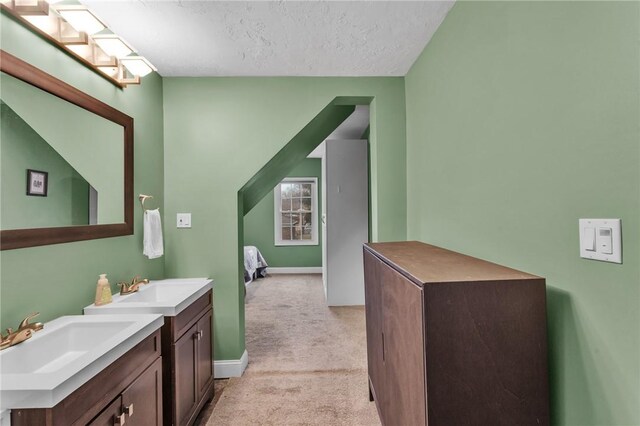 bathroom featuring a textured ceiling, baseboards, two vanities, and a sink