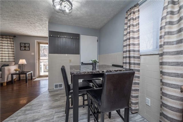 dining space featuring visible vents, wainscoting, wood finished floors, a textured ceiling, and tile walls