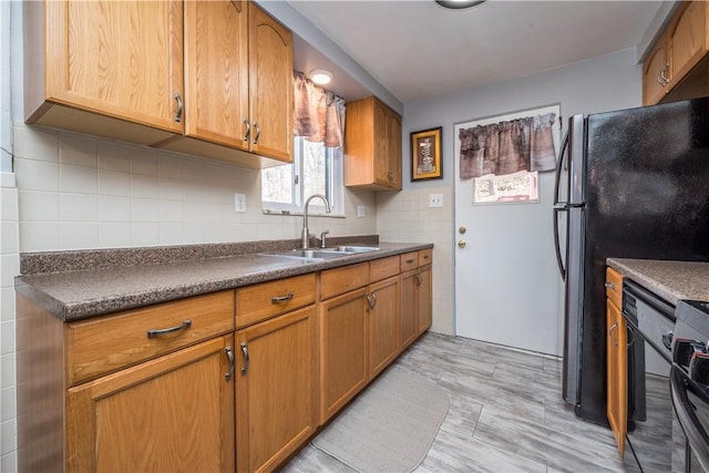 kitchen featuring dark countertops, freestanding refrigerator, brown cabinets, and a sink