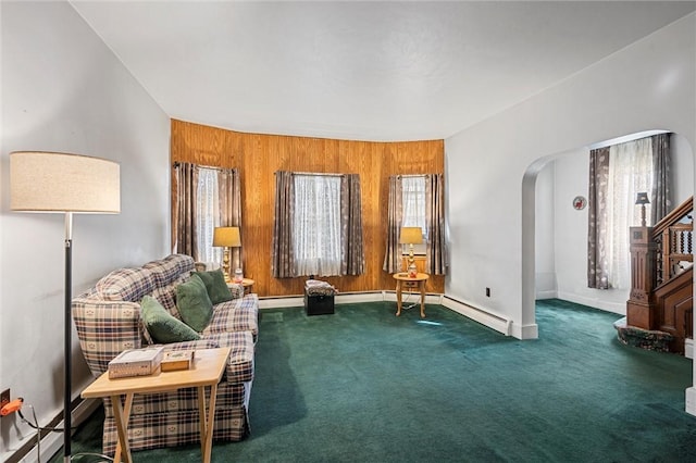 living area featuring arched walkways, a baseboard heating unit, wood walls, baseboards, and carpet