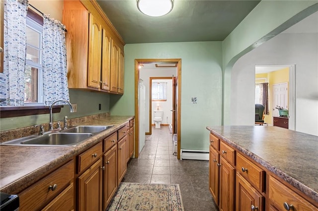 kitchen with arched walkways, brown cabinetry, a baseboard radiator, and a sink