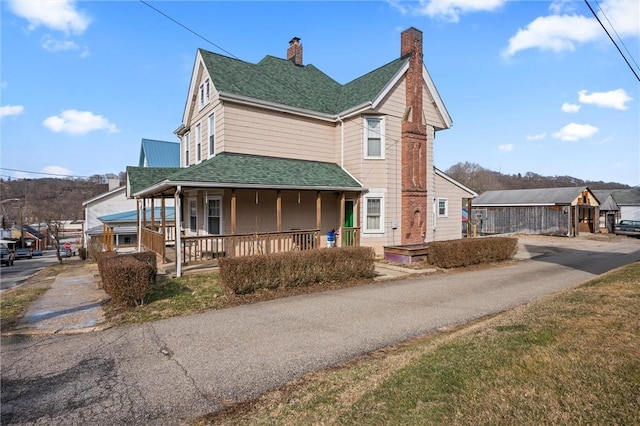 view of front of home featuring covered porch, a shingled roof, and a chimney