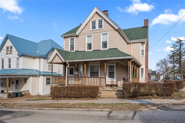 view of front of property featuring covered porch, roof with shingles, and a chimney