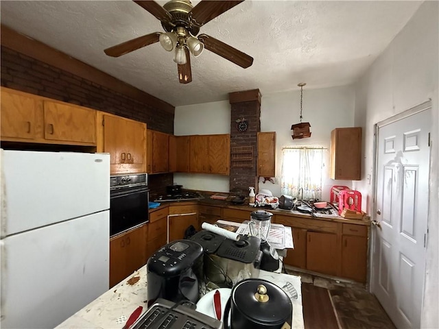 kitchen featuring a textured ceiling, black oven, freestanding refrigerator, brown cabinetry, and decorative light fixtures