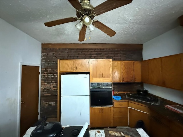 kitchen with a textured ceiling, stovetop, oven, and freestanding refrigerator