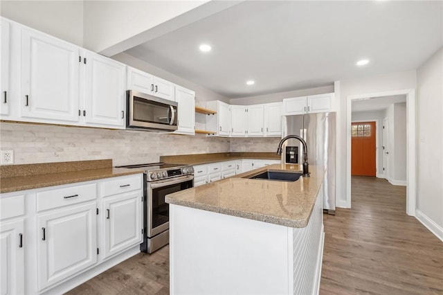 kitchen with light stone counters, wood finished floors, a sink, appliances with stainless steel finishes, and an island with sink