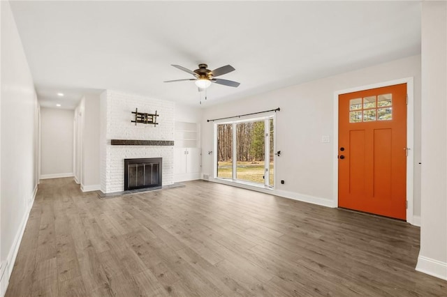 unfurnished living room featuring ceiling fan, a fireplace, wood finished floors, and baseboards