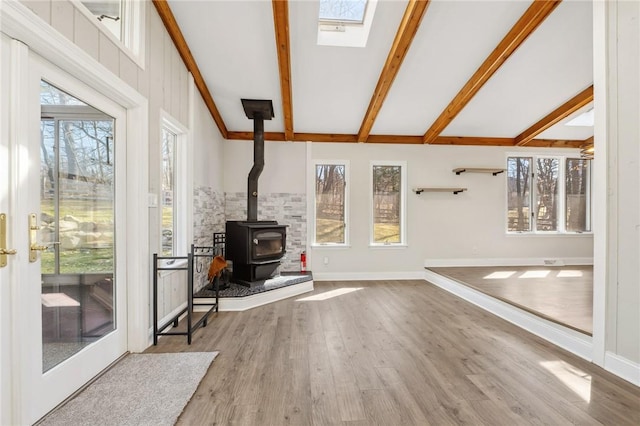 unfurnished living room featuring plenty of natural light, a wood stove, beamed ceiling, and wood finished floors