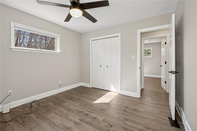 unfurnished bedroom with baseboards, visible vents, a ceiling fan, wood finished floors, and a closet