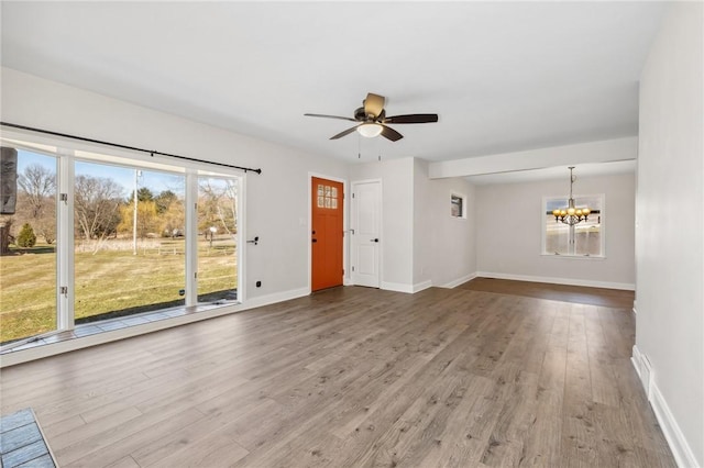 unfurnished living room with baseboards, wood finished floors, and ceiling fan with notable chandelier