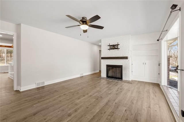 unfurnished living room featuring a brick fireplace, baseboards, visible vents, and wood finished floors