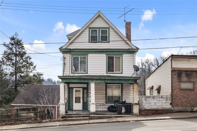 view of front facade featuring a porch, a chimney, and fence