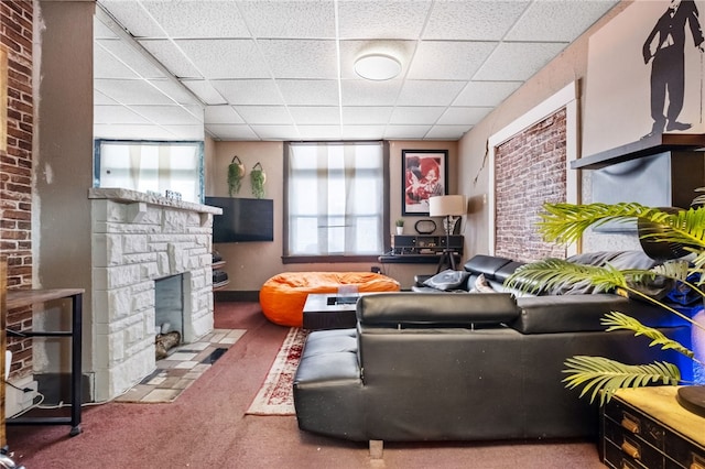 living room with a stone fireplace, carpet, and a drop ceiling