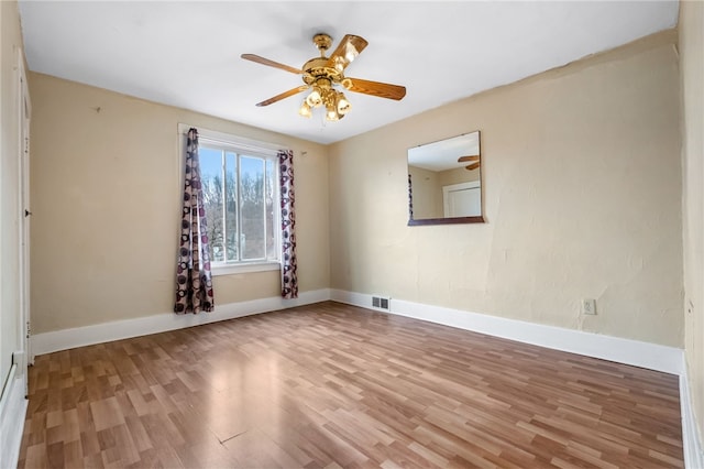 empty room with a ceiling fan, wood finished floors, visible vents, and baseboards