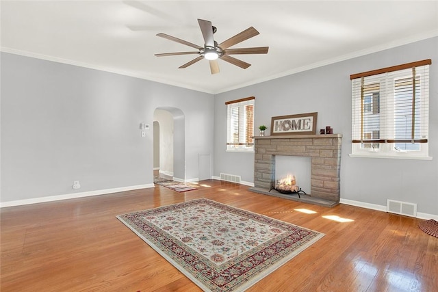 living area with arched walkways, a stone fireplace, wood finished floors, visible vents, and baseboards