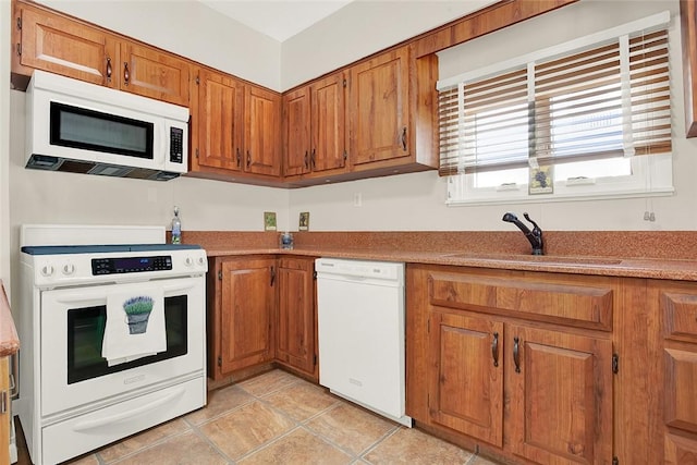 kitchen featuring brown cabinetry, white appliances, light countertops, and a sink