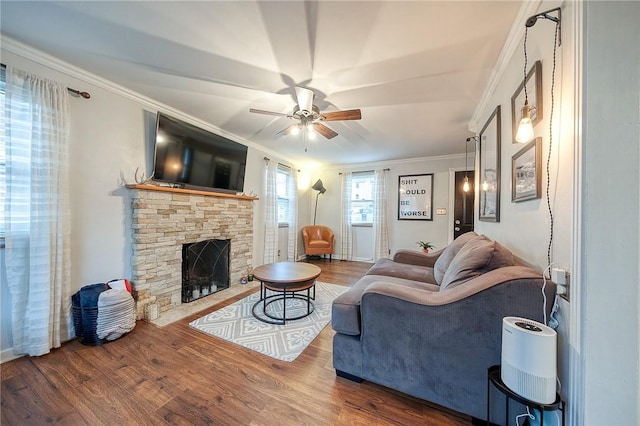 living area featuring a stone fireplace, ornamental molding, wood finished floors, and a ceiling fan