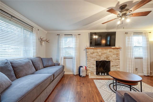 living room with crown molding, ceiling fan, wood finished floors, and a stone fireplace