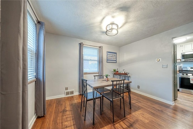 dining room featuring visible vents, a textured ceiling, baseboards, and wood finished floors