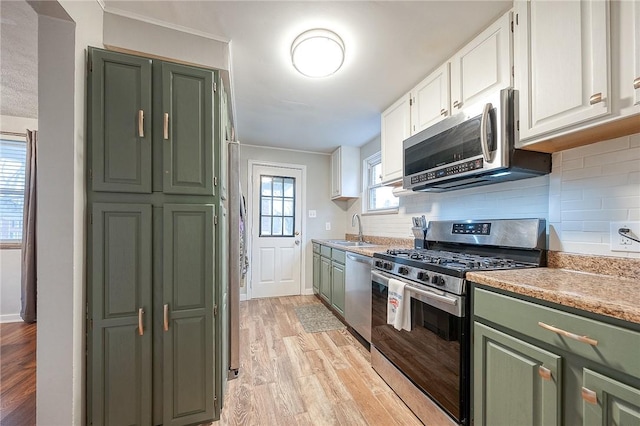 kitchen featuring stainless steel appliances, a sink, white cabinets, green cabinets, and light wood-style floors