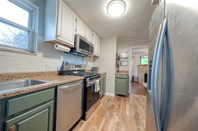 kitchen with decorative backsplash, appliances with stainless steel finishes, light wood-type flooring, white cabinetry, and green cabinets