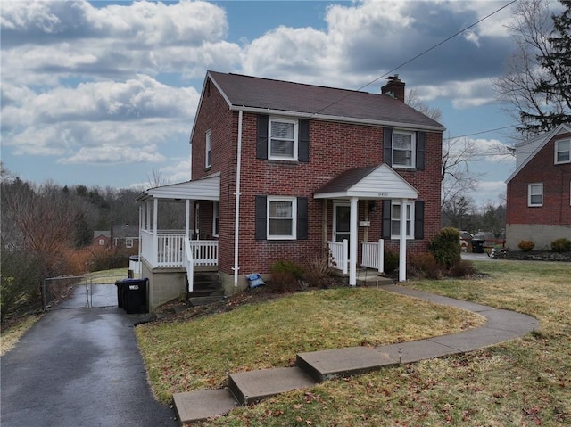 view of front facade featuring a front yard, a gate, brick siding, and a chimney