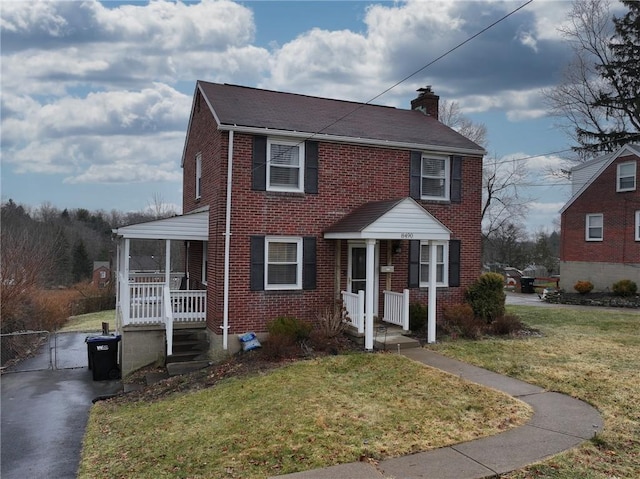 colonial home featuring brick siding, a chimney, a gate, a porch, and a front yard