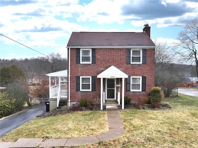 colonial house with brick siding, a chimney, and a front yard