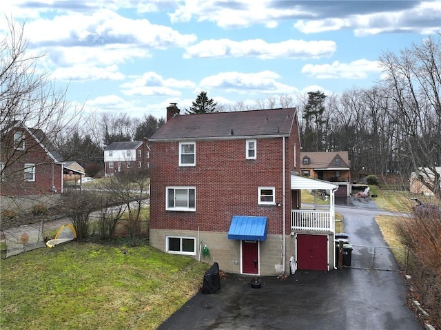 rear view of house with a chimney, aphalt driveway, a lawn, and brick siding