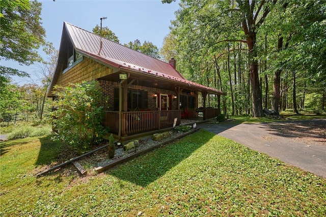 view of home's exterior featuring brick siding, a yard, a porch, a standing seam roof, and metal roof