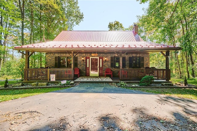 view of front of house featuring covered porch, a chimney, metal roof, and brick siding