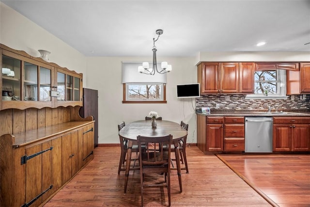 kitchen with light wood finished floors, decorative backsplash, dishwasher, brown cabinets, and an inviting chandelier