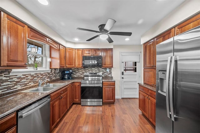 kitchen featuring wood finished floors, appliances with stainless steel finishes, brown cabinetry, and a sink