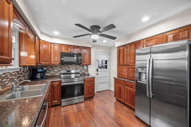 kitchen with stainless steel appliances, dark wood-type flooring, a sink, tasteful backsplash, and dark countertops