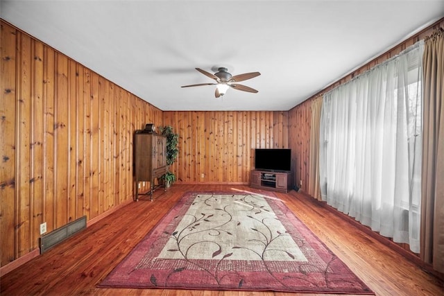 unfurnished living room with ceiling fan, wood finished floors, visible vents, and wooden walls