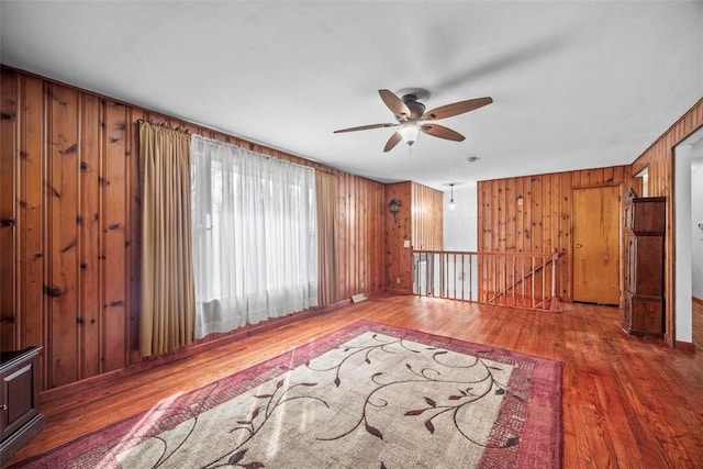 unfurnished living room featuring ceiling fan, wooden walls, and wood finished floors