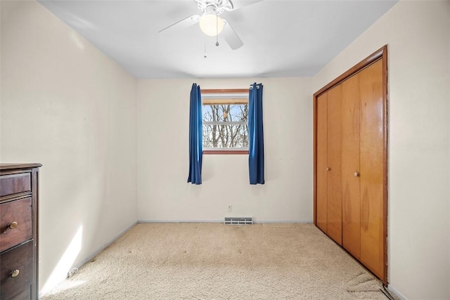 unfurnished bedroom with a closet, carpet, visible vents, and a ceiling fan