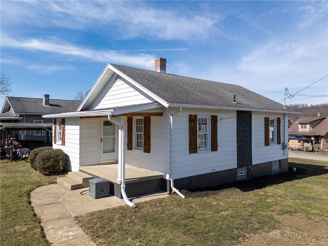 exterior space featuring a shingled roof, a chimney, and a front lawn