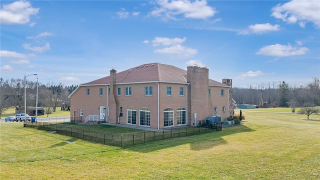 rear view of house with a lawn, a chimney, and fence