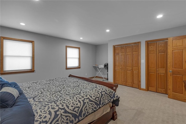 bedroom featuring light carpet, baseboards, multiple closets, and recessed lighting