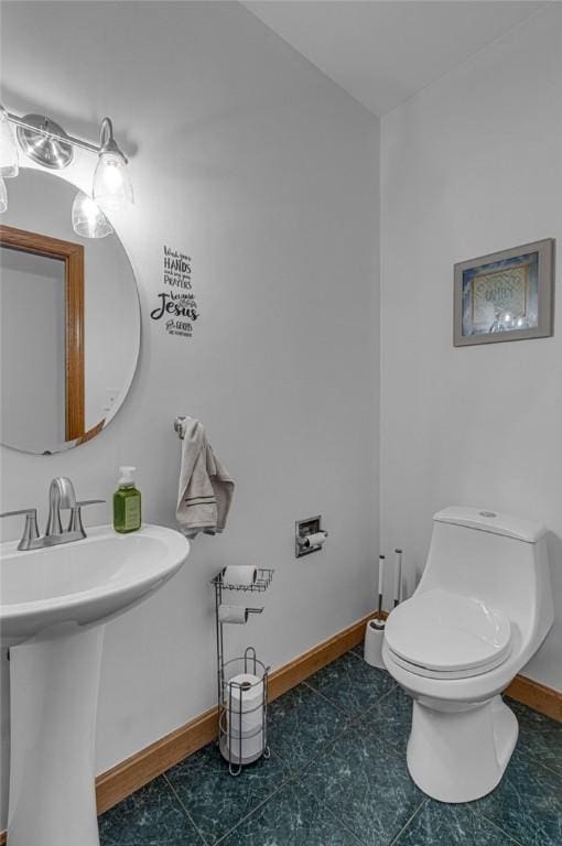 half bath with toilet, baseboards, and a sink