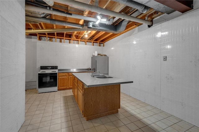 kitchen featuring stainless steel counters, electric range, freestanding refrigerator, a sink, and an island with sink