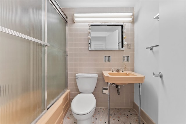 full bath with toilet, shower / bath combination with glass door, a sink, tile patterned flooring, and tile walls