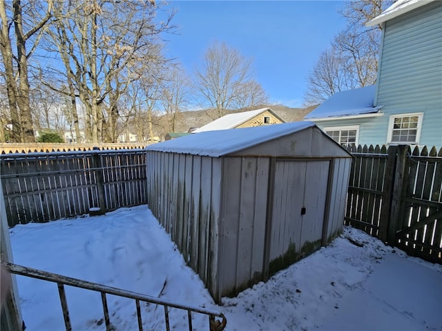 snowy yard with a fenced backyard, a storage unit, and an outdoor structure